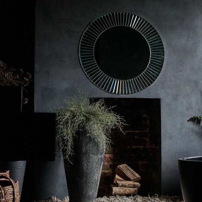 Large round mirror with a mirrored frame hung on a grey wall above a grey fireplace