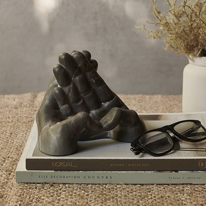 The Stony Phone Holder, a grey faux marble phone holder in the shape of two hands, sat on a stack of books.
