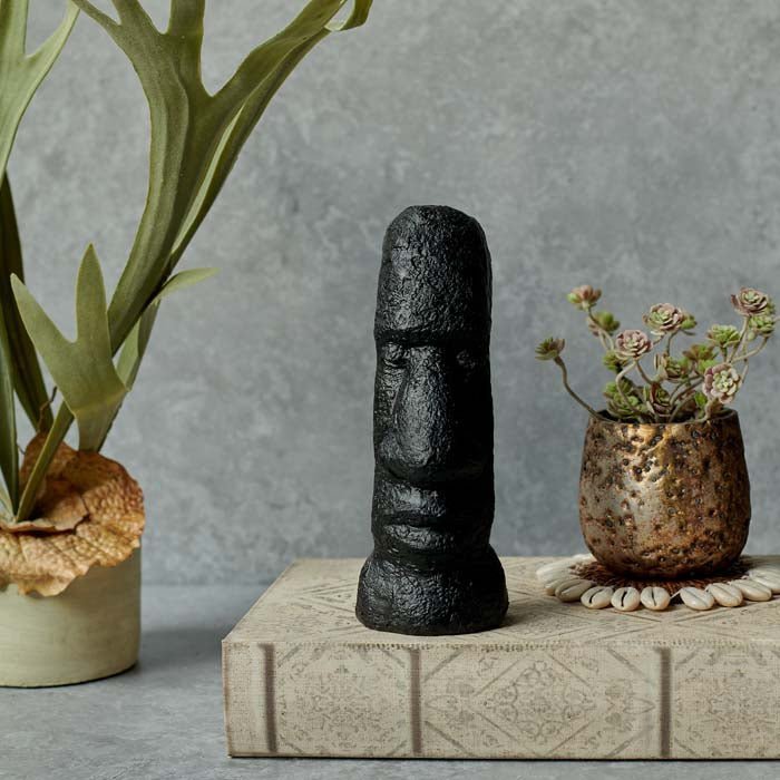 Long face sculpture in black sat on a book