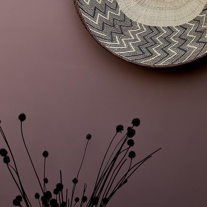 A rich pink painted wall with a decorative woven basket hanging from it