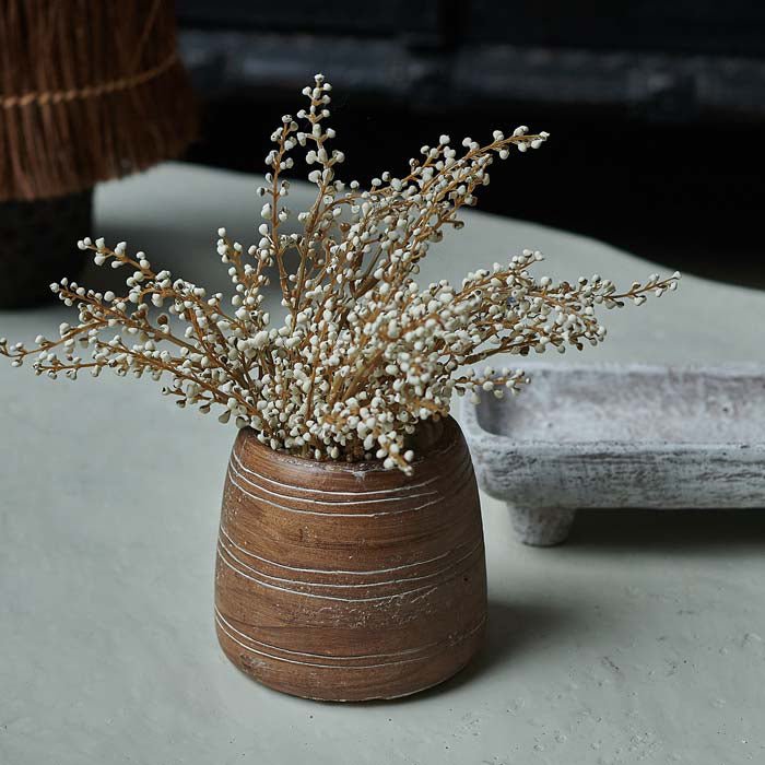 Artificial white heather foliage in a brown wood-effect cement vase.