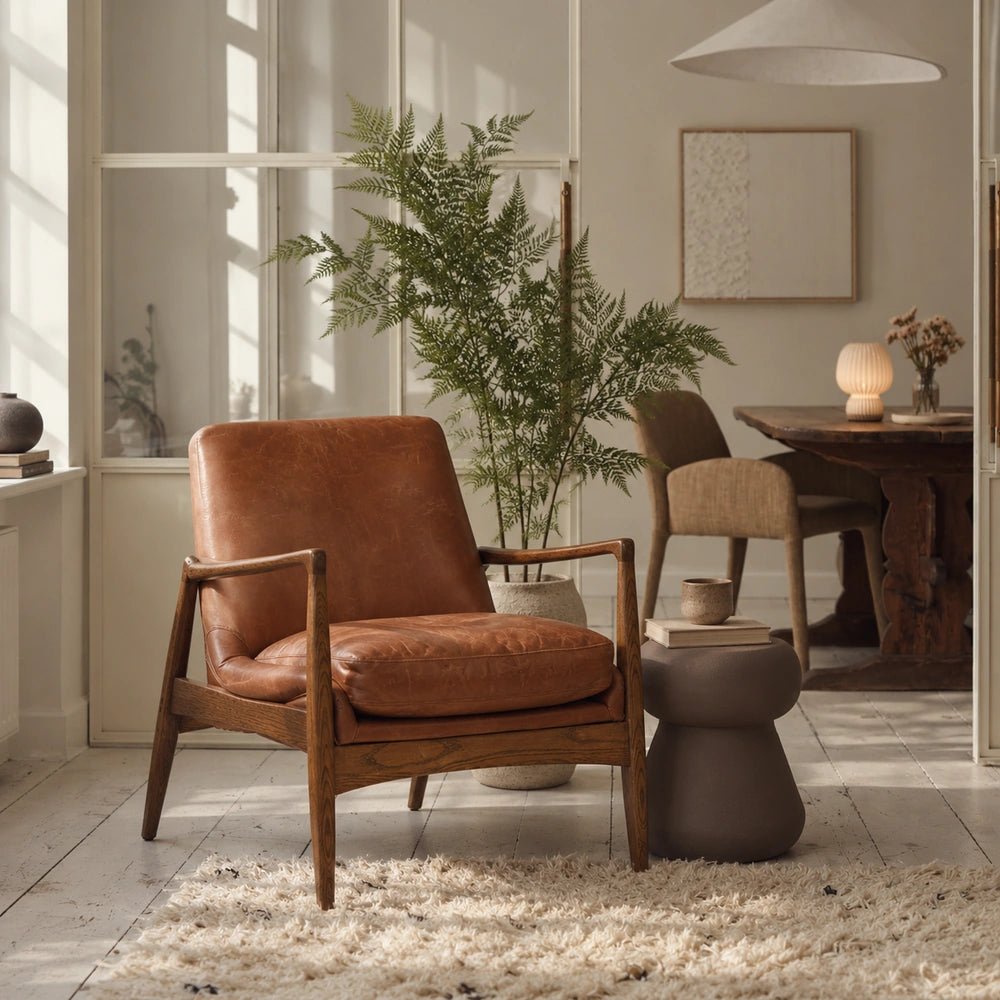Truman Brown Leather Armchair with warm leather upholstery and exposed wooden frame, styled in a light neutral living room beside plants and side tables.