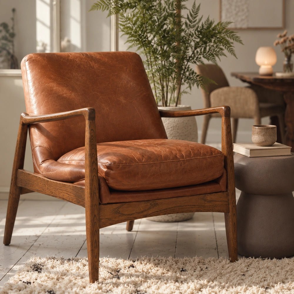 Truman Brown Leather Armchair with warm leather cushions and exposed wooden frame, styled in a bright living room with plants and neutral furnishings.
