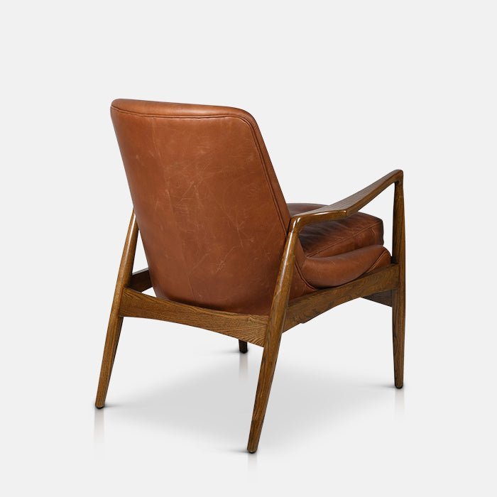 Abigail Ahern Truman Brown Leather Armchair in dark brown leather with a curved backrest, generously cushioned seat and ash wood frame, creating a warm and timeless focal point in a modern living space.