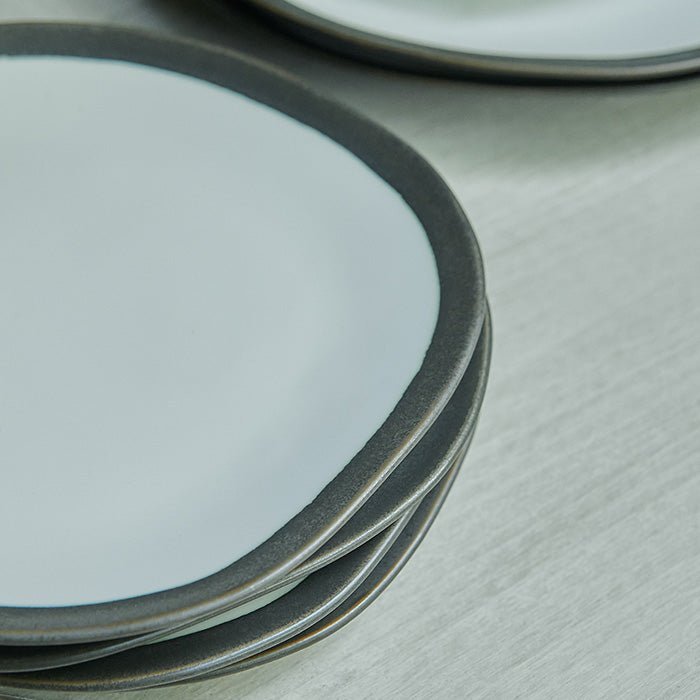 A close up of the Truman Stoneware Dinner Set - 12 Piece. A set of white organic shaped tableware with a stylish black rim.