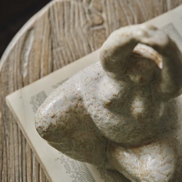 A cream ceramic sculpture of seated female yoga lady with crossed legs and her arms raised above her head style on a coffee table to create a unique vignette.
