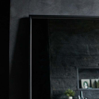 A large rectangular mirror with a thin black metal frame and rounded corners. Leaning against a grey tadelakt wall. A great mirror for a small bathroom.