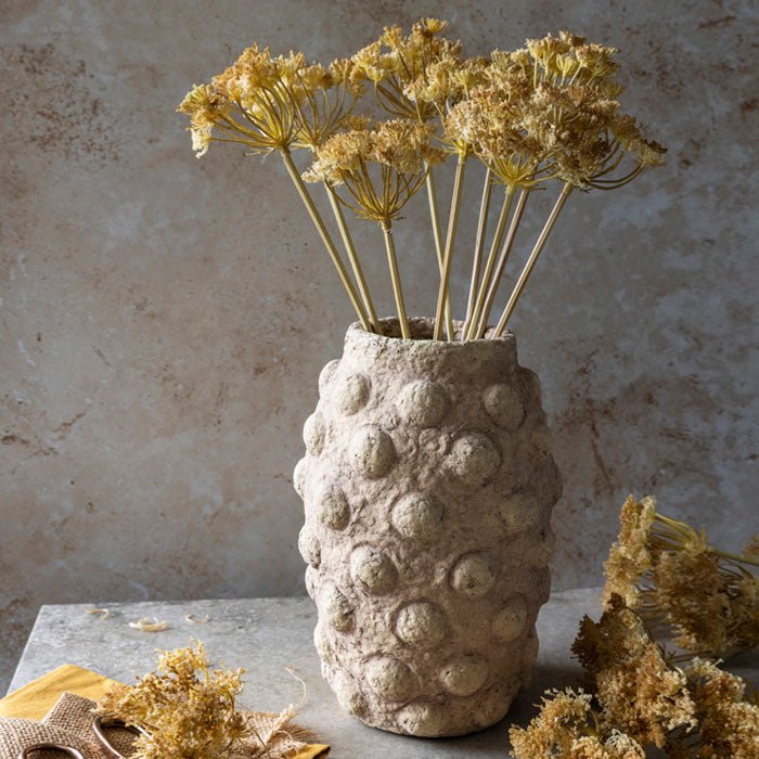 A large beige cement vase with a bobble texture holding some artificial flowers.