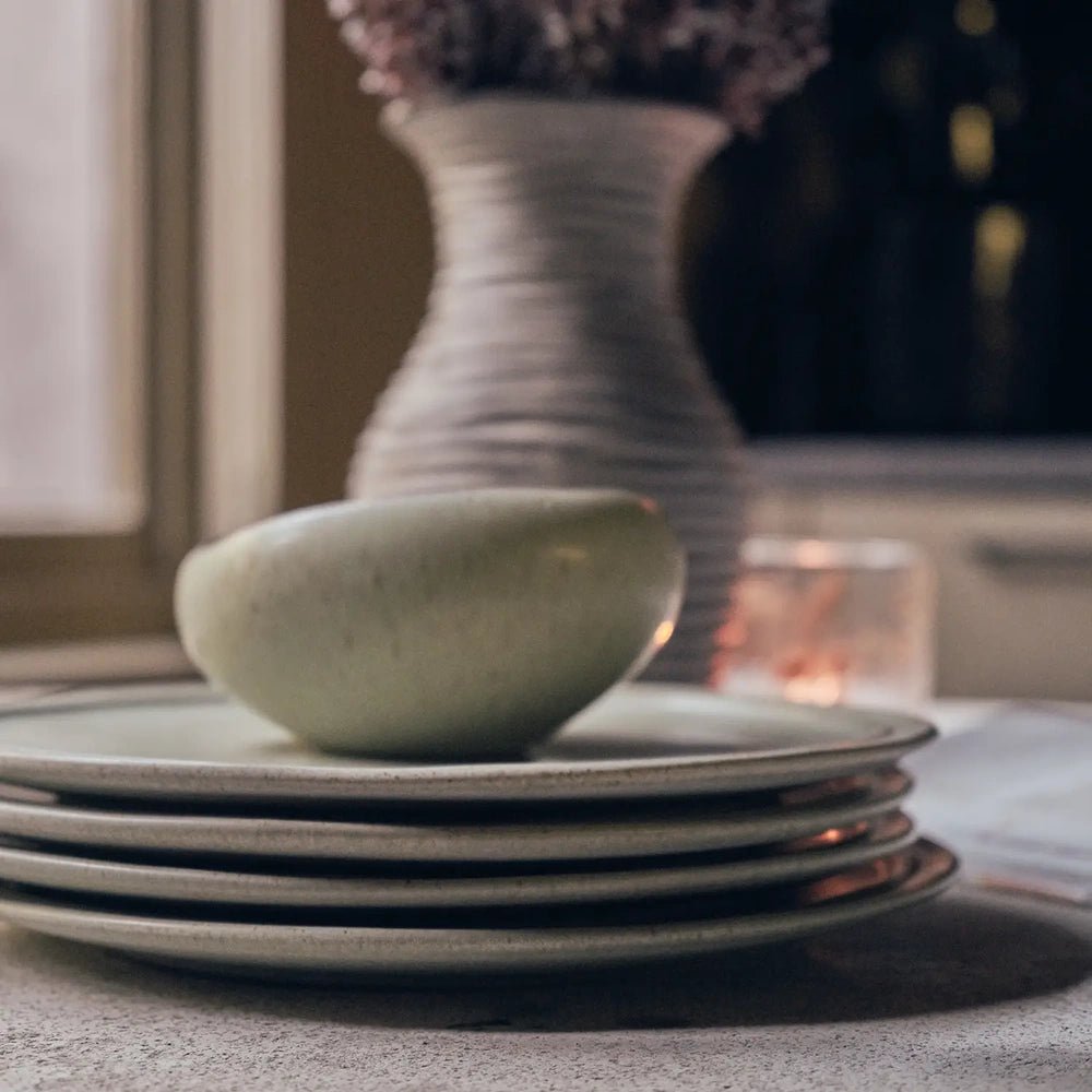 Alcott 12-Piece Dinner Set shown from the side, with a rounded green bowl resting on stacked plates, emphasizing raised rims and softly speckled surfaces.