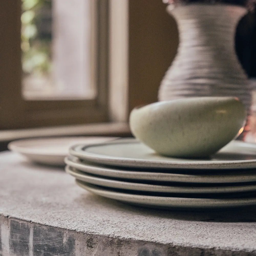 Alcott 12-Piece Dinner Set shown in close up with a rounded green bowl above stacked plates, highlighting their curved profiles, speckled surfaces and raised rims.