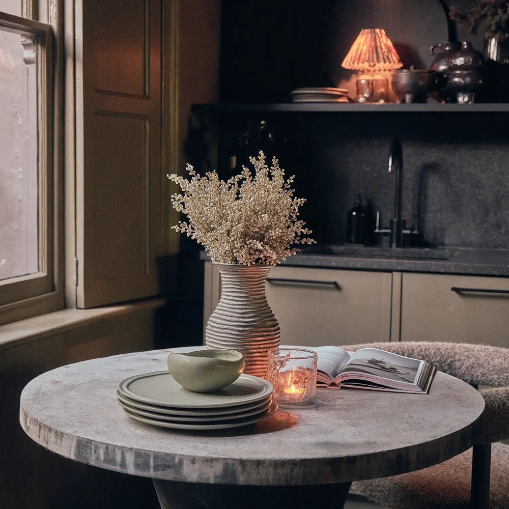 Alcott 12-Piece Dinner Set arranged as stacked green plates topped by a rounded bowl on a round kitchen table, with candlelight and an open book.