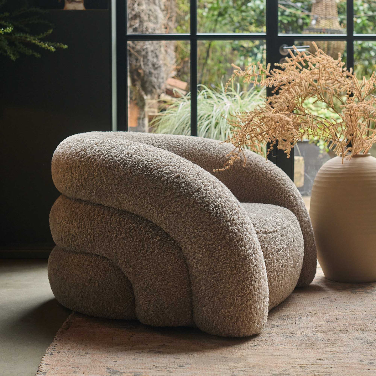 Neutral curved armchair with a plush upholstered finish, rounded silhouette and deep comfortable cushioning. Almar Curved Armchair by Abigail Ahern, designed with a warm earthy tone and contemporary shape to create a stylish statement seating piece. A luxury accent chair perfect for living rooms, bedrooms and cosy reading spaces, adding texture, comfort and timeless elegance to modern home interiors.