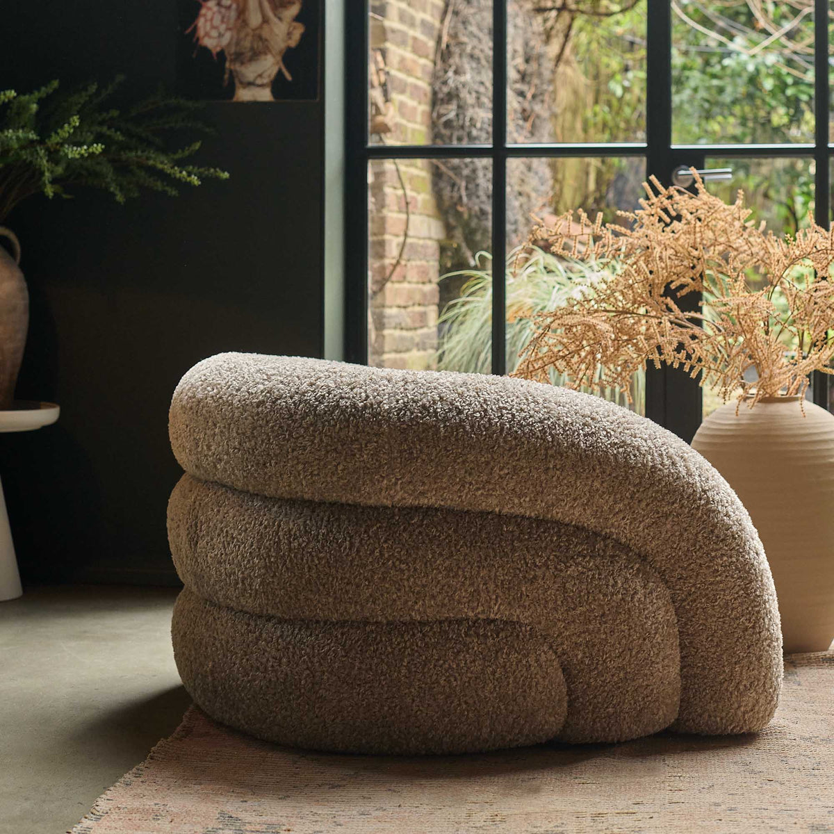 Neutral curved armchair with a plush upholstered finish, rounded silhouette and deep comfortable cushioning. Almar Curved Armchair by Abigail Ahern, designed with a warm earthy tone and contemporary shape to create a stylish statement seating piece. A luxury accent chair perfect for living rooms, bedrooms and cosy reading spaces, adding texture, comfort and timeless elegance to modern home interiors.