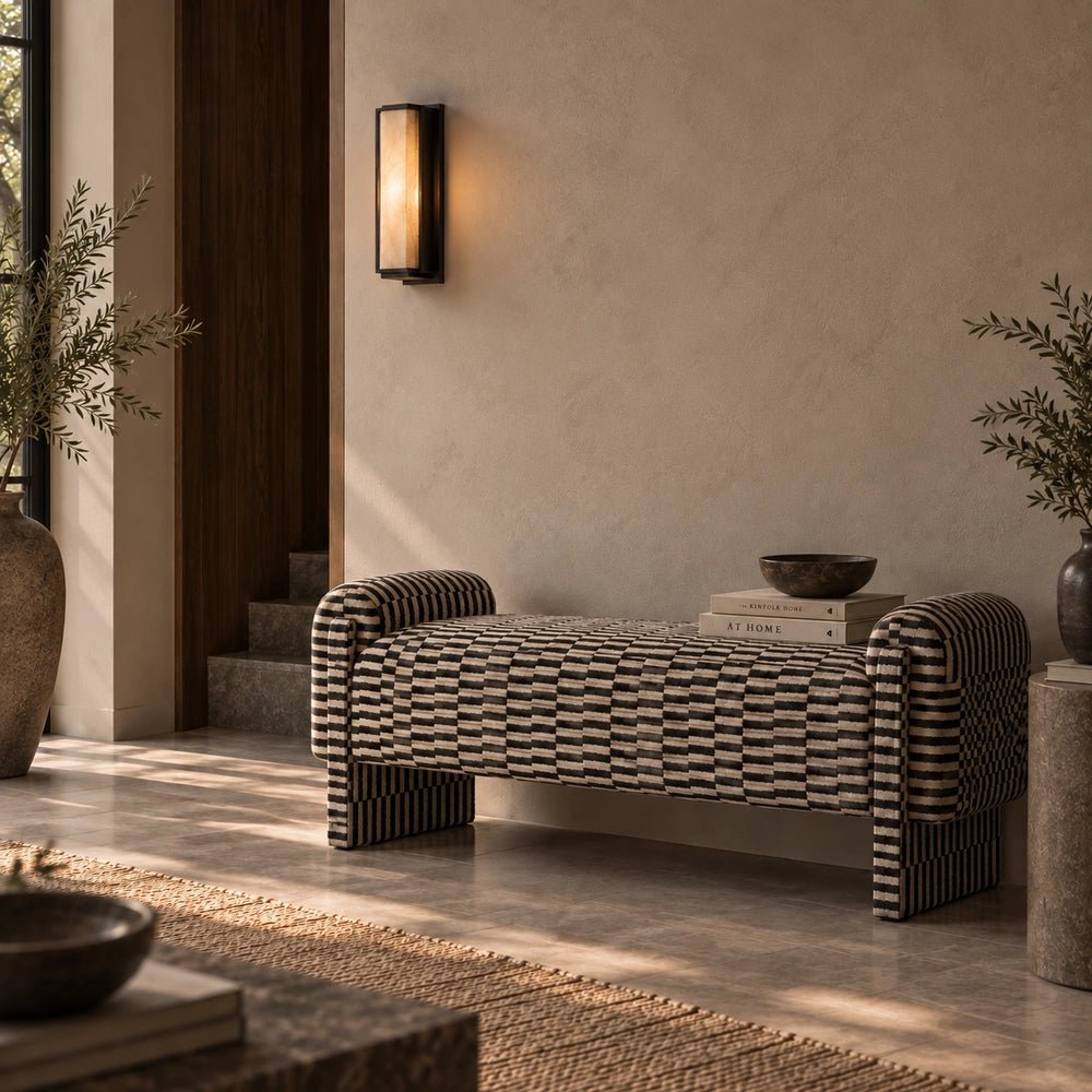 Alvarez Upholstered Bench styled in a warm hallway, showing its sculptural curved ends and richly textured woven upholstery beside a wall light and decorative bowl.