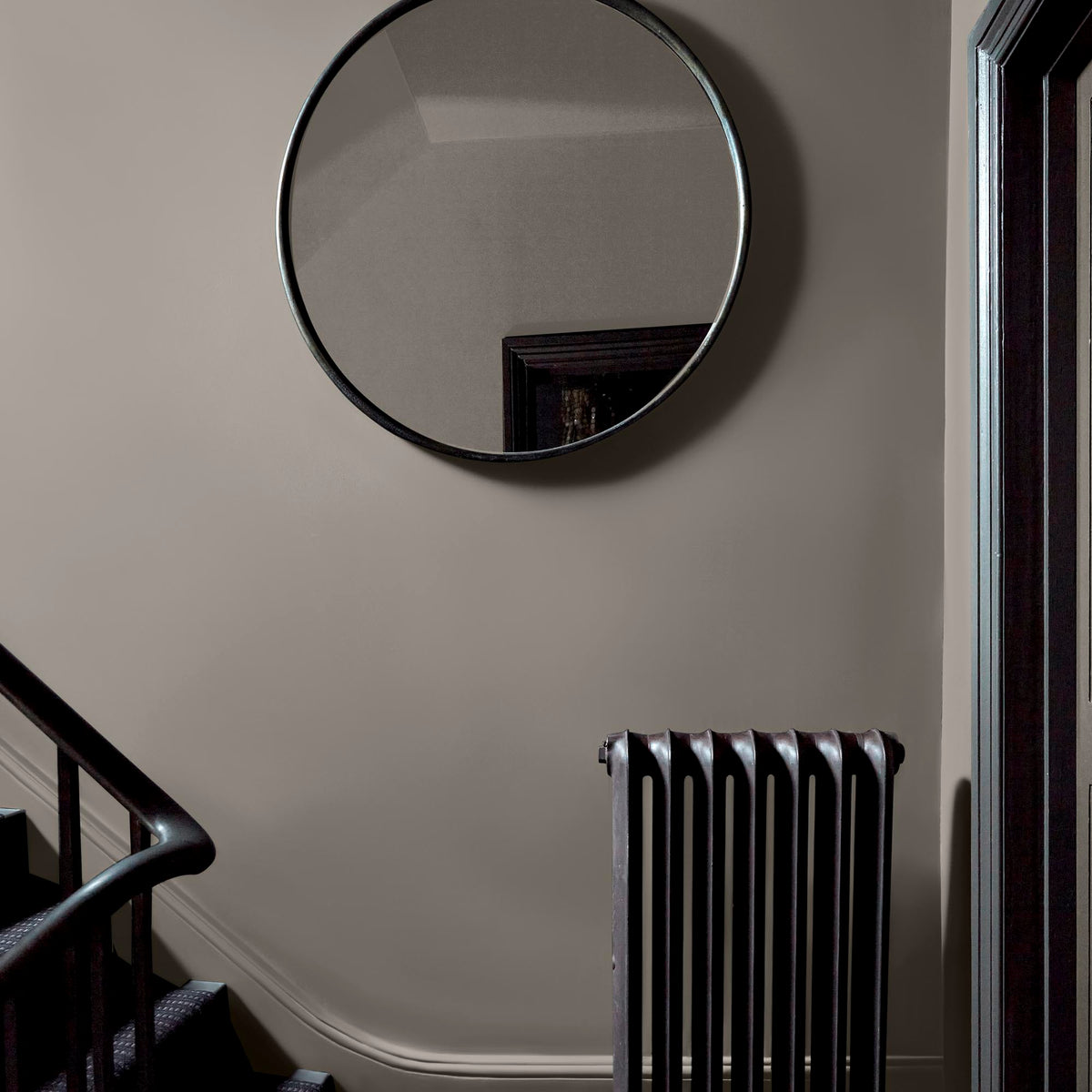 A staircase landing with a large circular mirror and walls painted in a light greige paint colour with beige undertones.