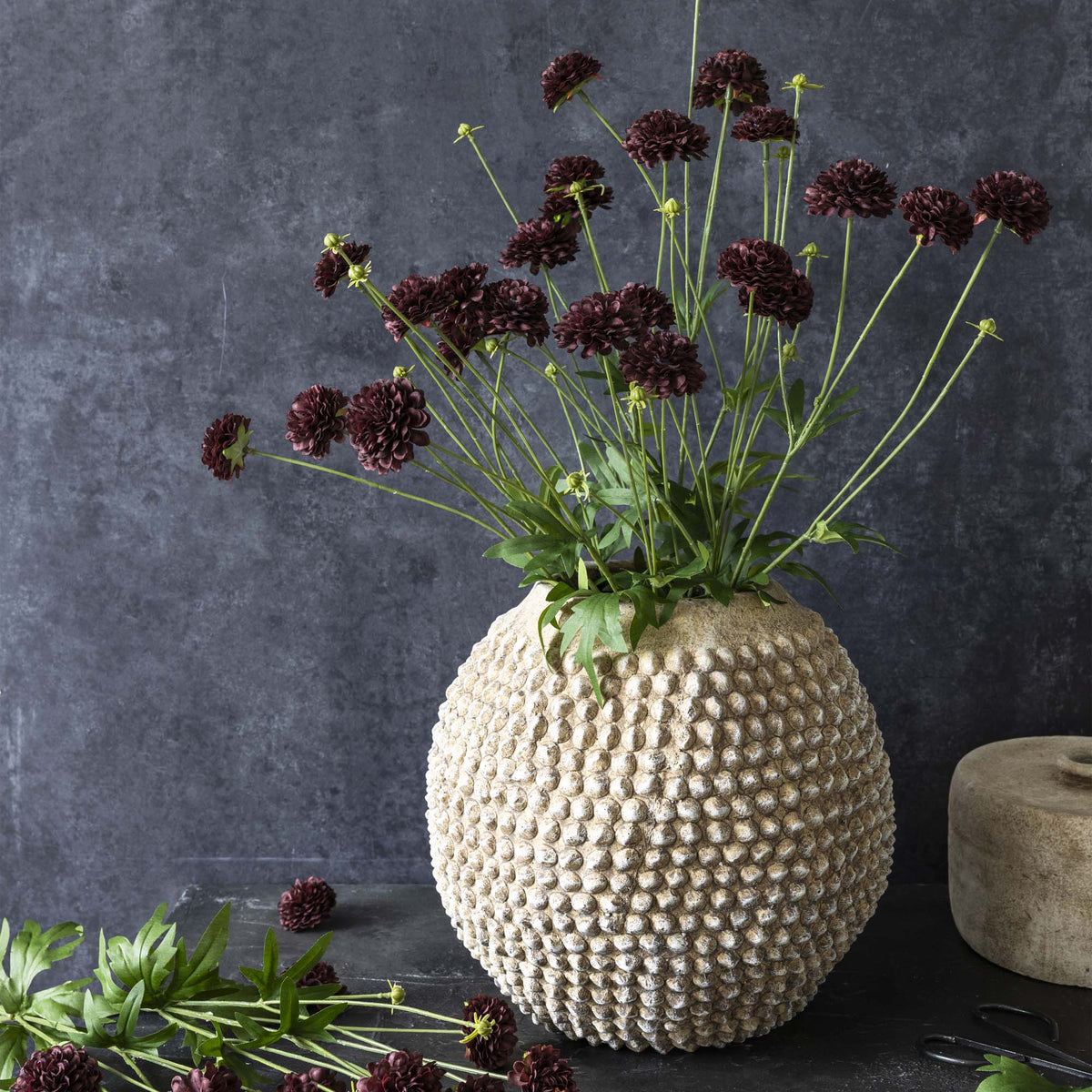 Textured vase with dark flowers against a dark gray background