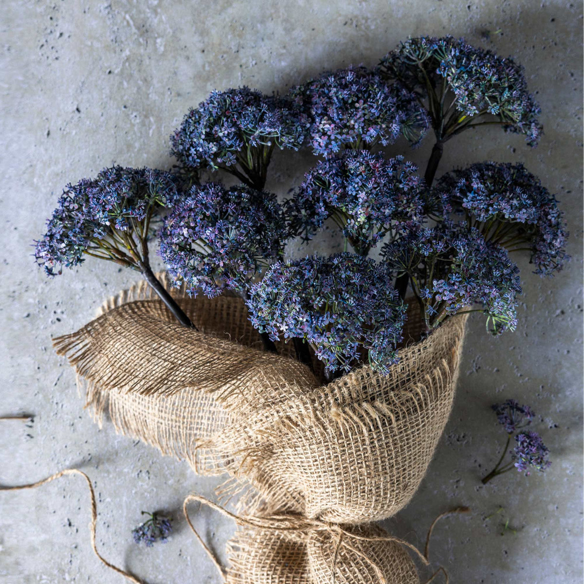 A floral bouquet of blue artificial flowers wrapped in burlap.