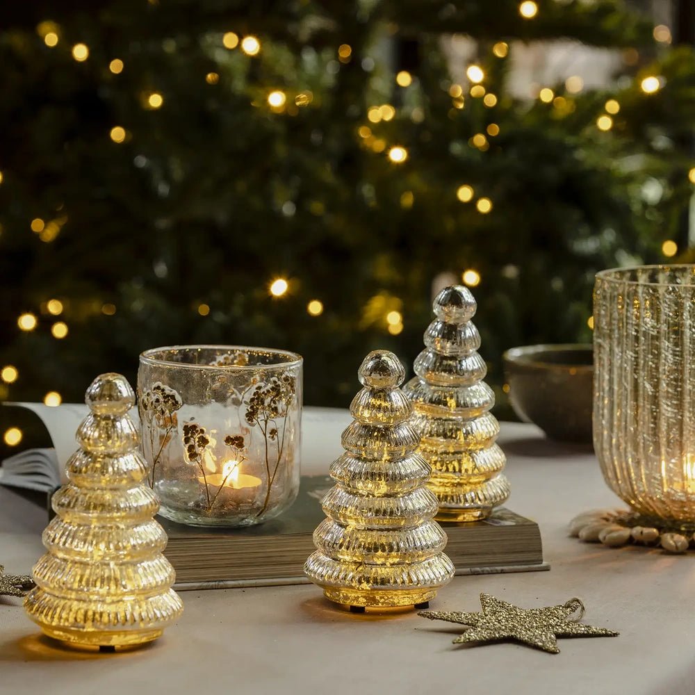 Aurora silver tree portable lamps with rounded finials and tiered ribbed bodies glow beside a candleholder, book and star ornaments against Christmas tree lights.