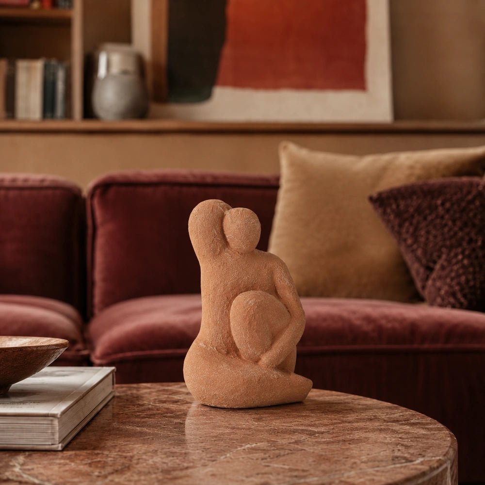 Aveline Figurative Sculpture in warm terracotta tones, centred on a round wooden coffee table before a rust velvet sofa and layered cushions.