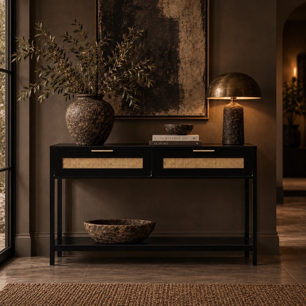 Bailey Wood Console Table styled in a warm hallway, with black frame, woven cane drawer fronts, brass handles, books, lamp and decorative vase.