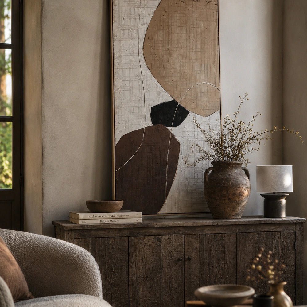 Balance Painting displayed above a rustic wooden sideboard in a warm neutral interior, styled with books, a textured vase, branches and a table lamp.