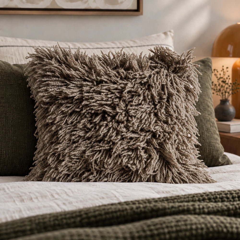 Barmount Textured Cushion in slate grey textured fabric, styled in a layered living room setting with neutral upholstery and warm decorative accents.