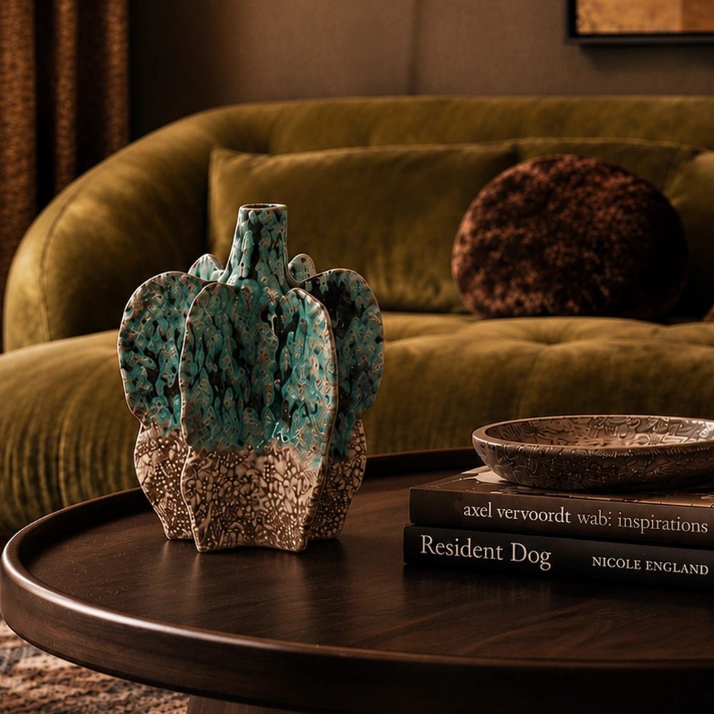 Bellamy Stoneware Vase with sculptural ridged form and mottled green surface, styled on a dark tray beside stacked books and an olive green sofa.