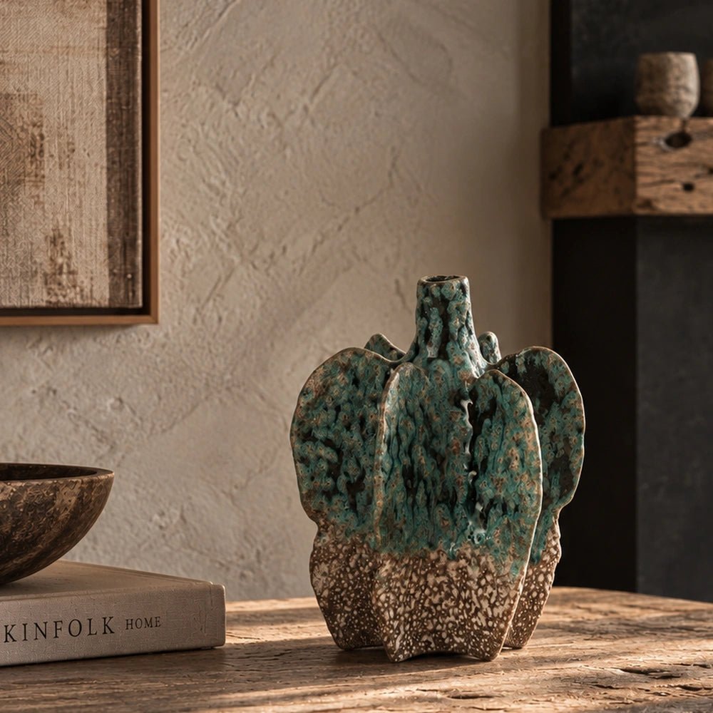 Bellamy Stoneware Vase with sculptural ridged form and mottled green surface, displayed on a pale stone console beside stacked books and neutral decorative objects.