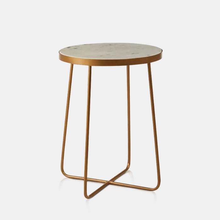 A cutout of the Blanco Marble Side Table, a small round table with an off-white marble top and slim gold legs in an X shape.