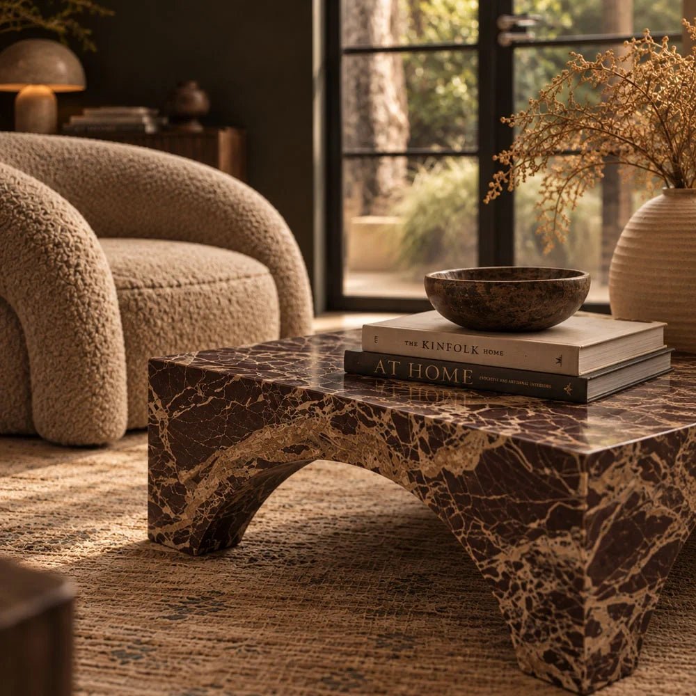 Braddow Marble Coffee Table with brown and cream veining, styled with books and a shallow bowl beside a rounded cream armchair and window.