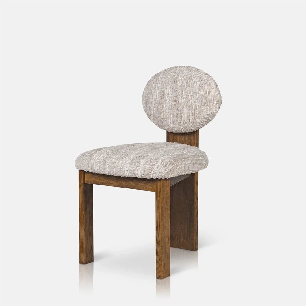 Channing boucle dining chair viewed at an angle, with a circular cream textured backrest, upholstered seat and angular wooden frame with warm brown legs.