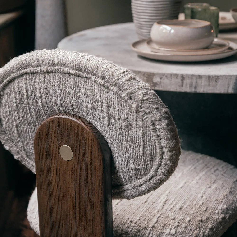 Channing boucle dining chair shown close up, highlighting its curved cream textured backrest, wooden rear support and upholstered seat beside a round dining table.