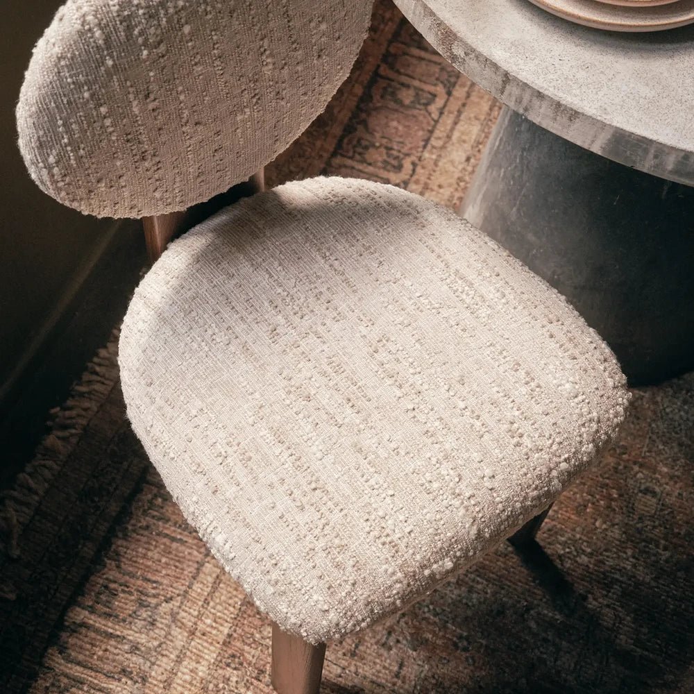 Channing boucle dining chair viewed from above, highlighting its rounded cream textured seat, circular upholstered back and wooden frame beside a stone dining table.