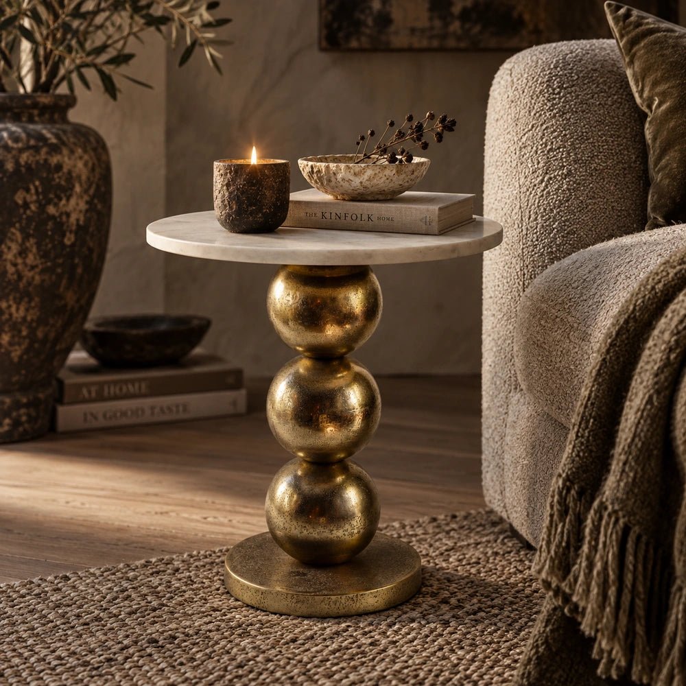 Chelsea Marble Side Table styled beside a dark sofa, topped with books and glassware in a moody lounge with sculptural lighting and art.