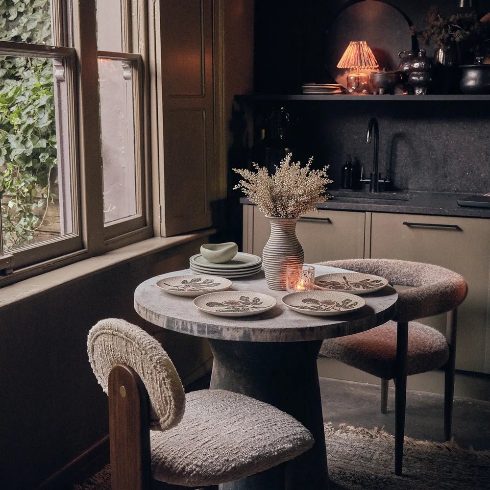 Corbett Mosaic Dinner Plates feature botanical patterns in muted colours, arranged with bowls and glassware on a round dining table beside a window.