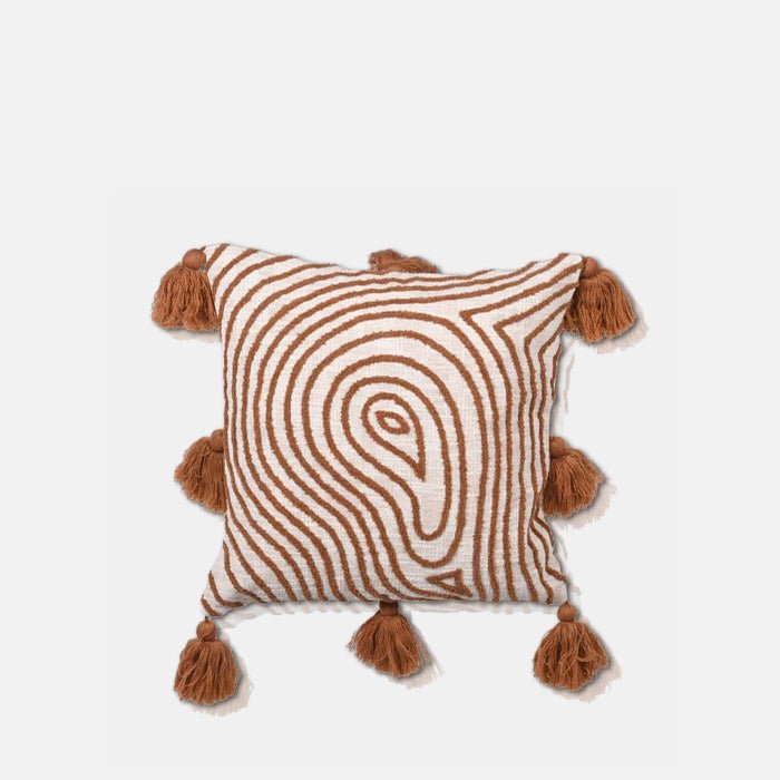 Cutout of the Demelza Embroidered Cushion, a square cream coloured cushion with a radiating organic pattern and tassels in terracotta.