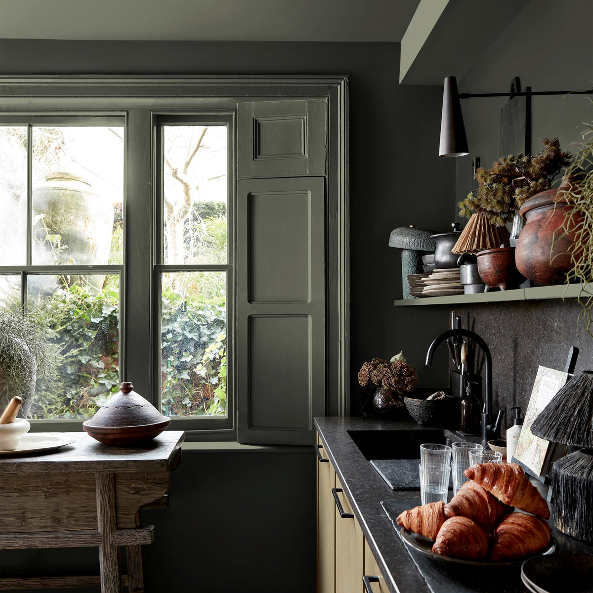 Abigail Ahern Desert Saltbush paint – a sumptuous dark olive green on kitchen window shutter and wall, beautifully offset by a sleek black countertop