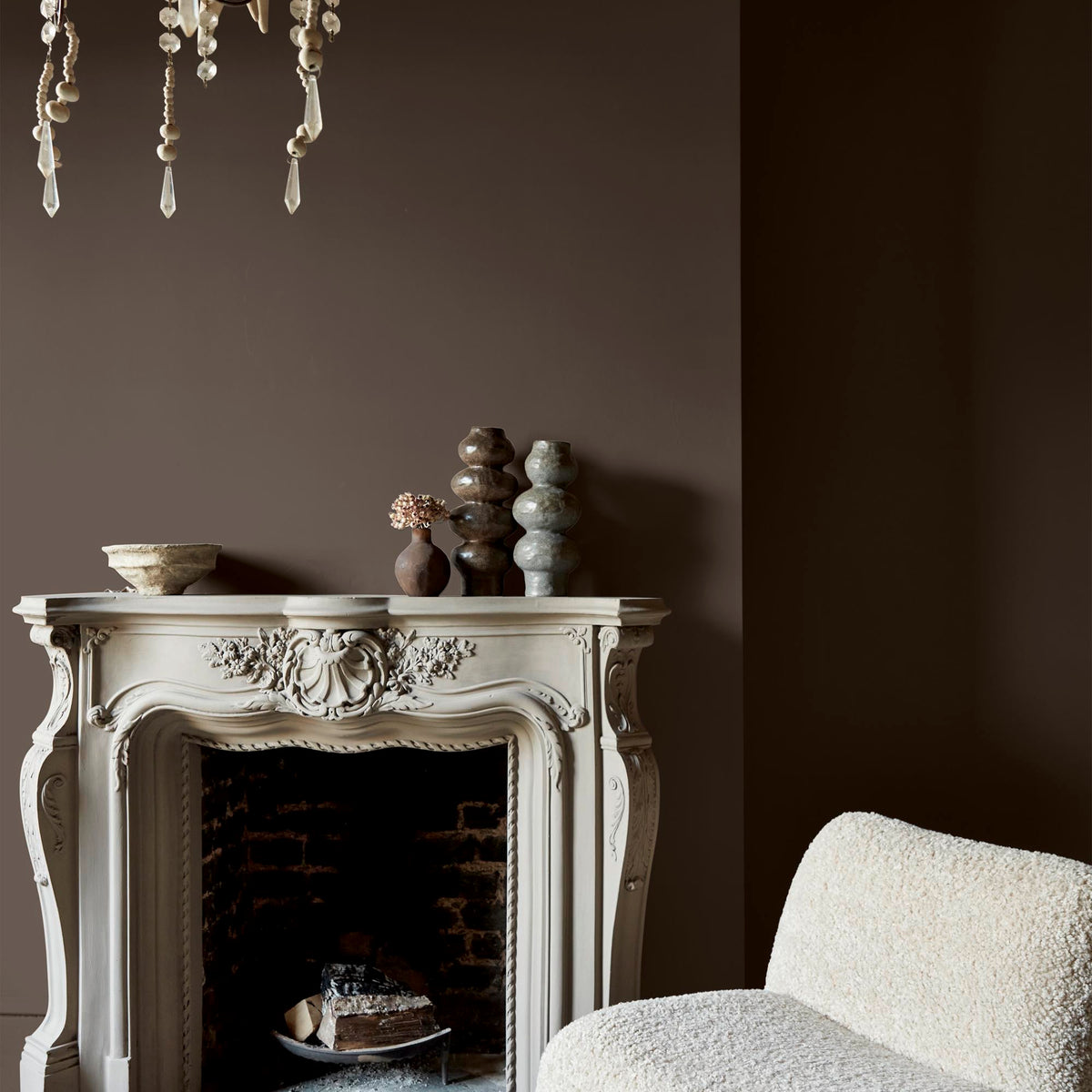 Abigail Ahern Dewdrop Moss paint – a sumptuous deep brown with warm undertones enveloping a beautifully styled fireplace setting with ceramic vases and accent chair