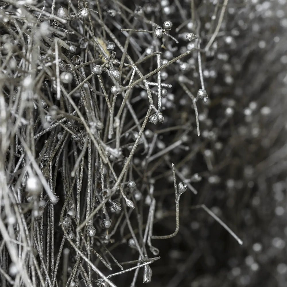 Dried gypsophilia wreath shows overlapping grey branches with small pale buds in close view, highlighting its fine angular structure against a softly blurred dark background.
