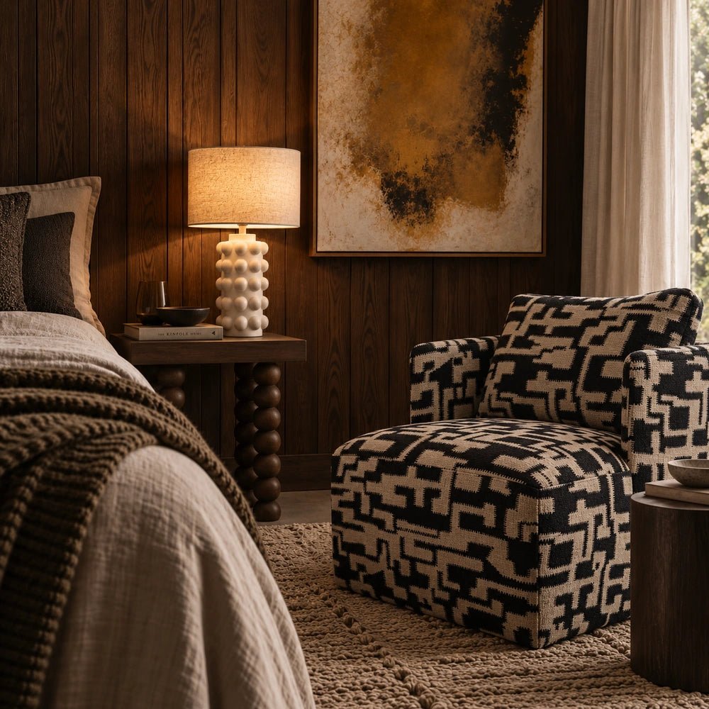 Dulwich Patterned Armchair with bold black and beige geometric upholstery positioned beside a bed in a warm, layered neutral bedroom.