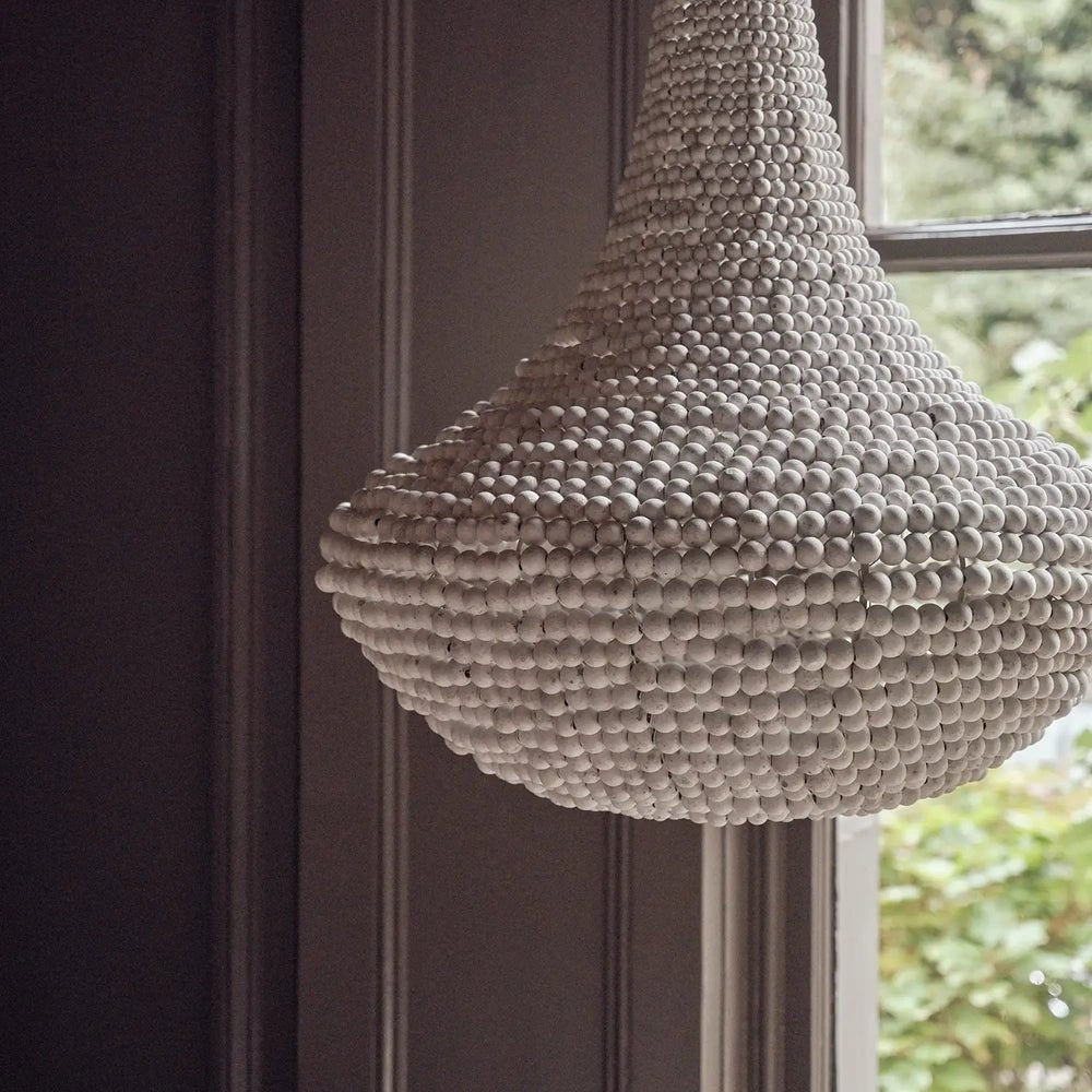 Eloise Beaded Chandelier features layered rows of pale beads forming a rounded pendant, suspended beside a window against dark panelled walls.