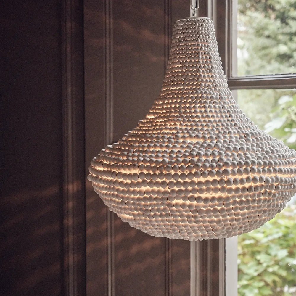 Eloise Beaded Chandelier glows through rows of pale beads, highlighting its curved shape beside a window and dark panelled interior walls.