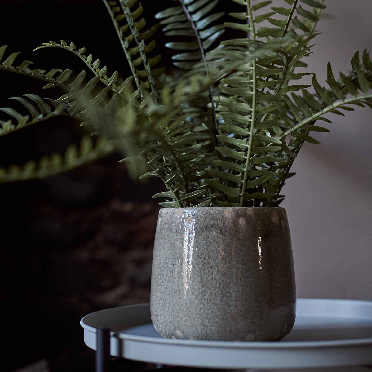 The Artificial Fern in Khaki Pot, a tall faux potted fern in a glossy khaki coloured glazed ceramic pot on a side table.