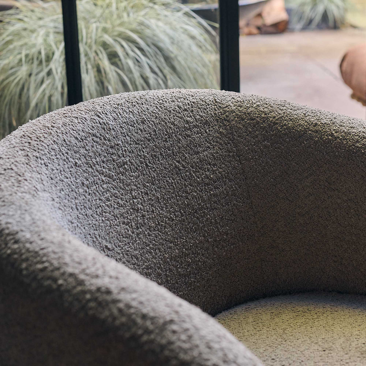 Close up of a Taupe swivel armchair with a soft textured fabric, sculptural curved silhouette and concealed 360-degree swivel base. Harper Swivel Armchair by Abigail Ahern, designed to bring effortless comfort and flexible seating to modern living rooms, bedrooms and reading corners. A contemporary accent chair that moves with your space, adding warmth, texture and timeless style to luxury home interiors.