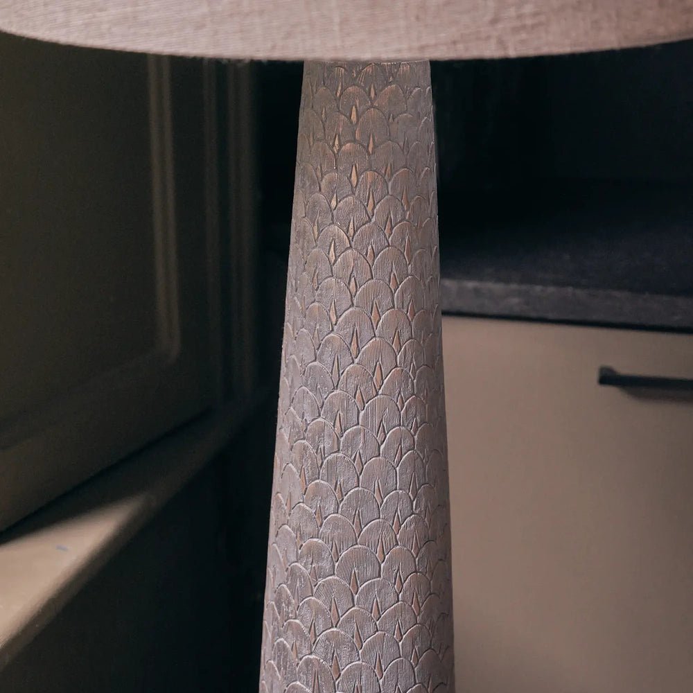 Haverford Polyresin Floor Lamp detail highlights the raised repeating pattern on its tapered base beneath a pale fabric shade, viewed in a warm interior.