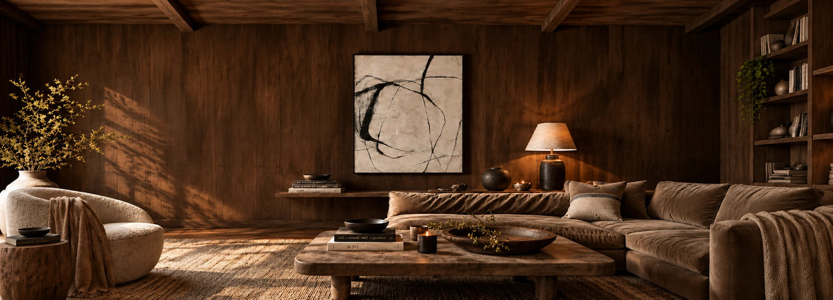 Large framed abstract artwork with black sweeping lines on a cream background, displayed above a brown sofa in a warmly lit, wood-panelled living room.