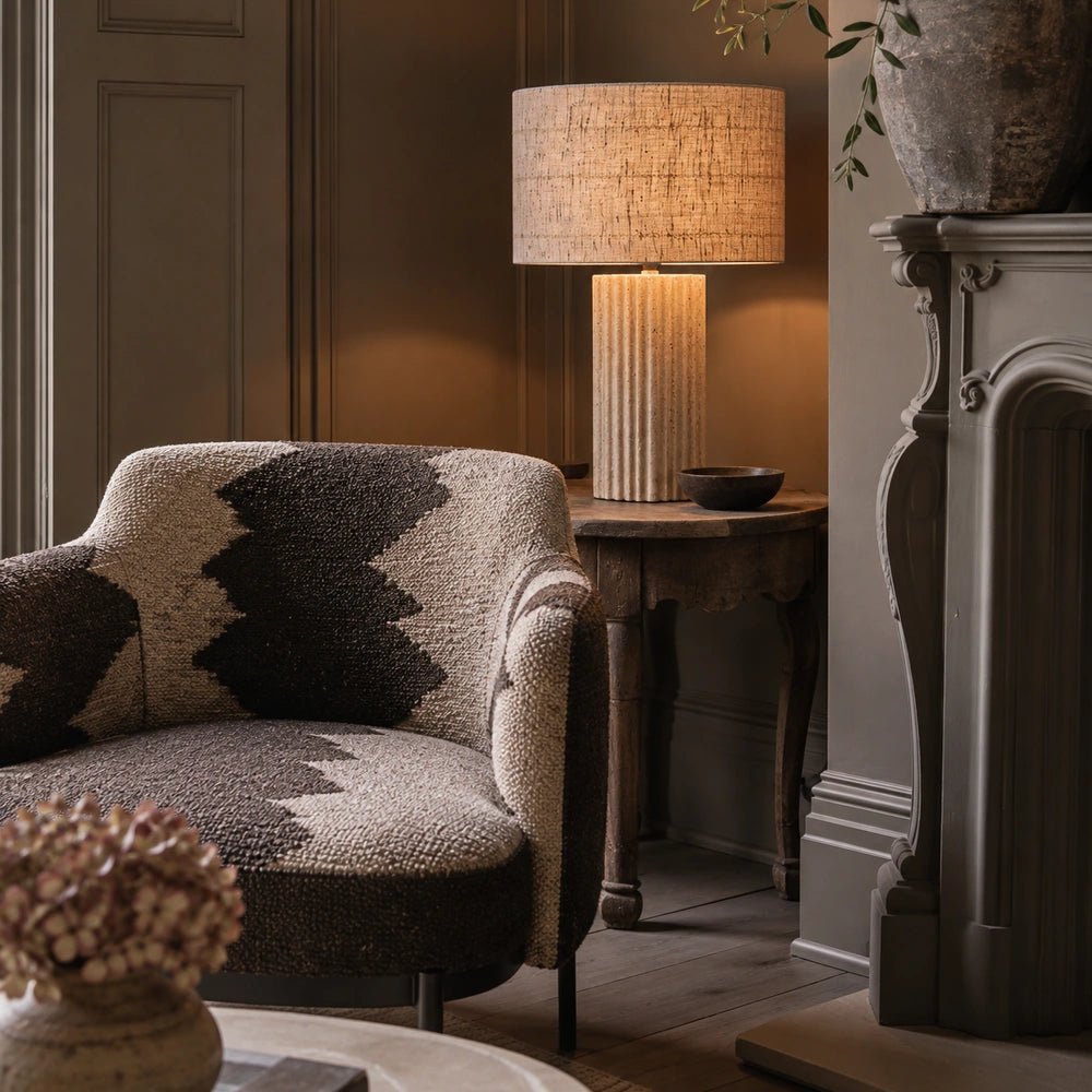 Hurdcott Travertine Table Lamp with textured stone base and pale shade, styled on a side table with books and decorative objects in a warm room.