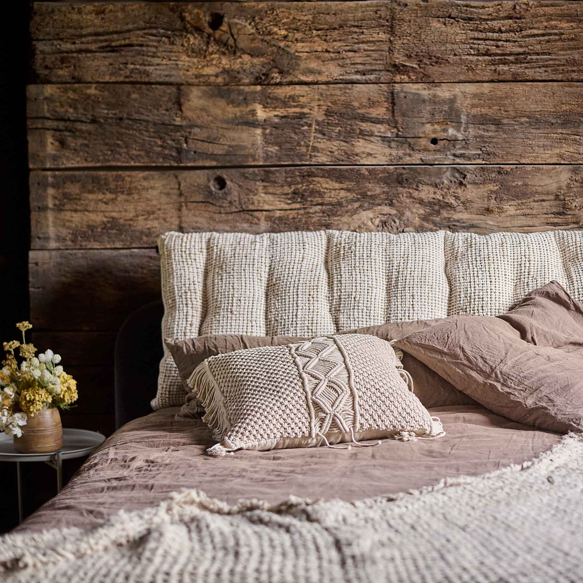 The Konta Headboard Cushion, a long rectangular sumptuous padded cushion in woven jute and cushion, on a cosy bed.