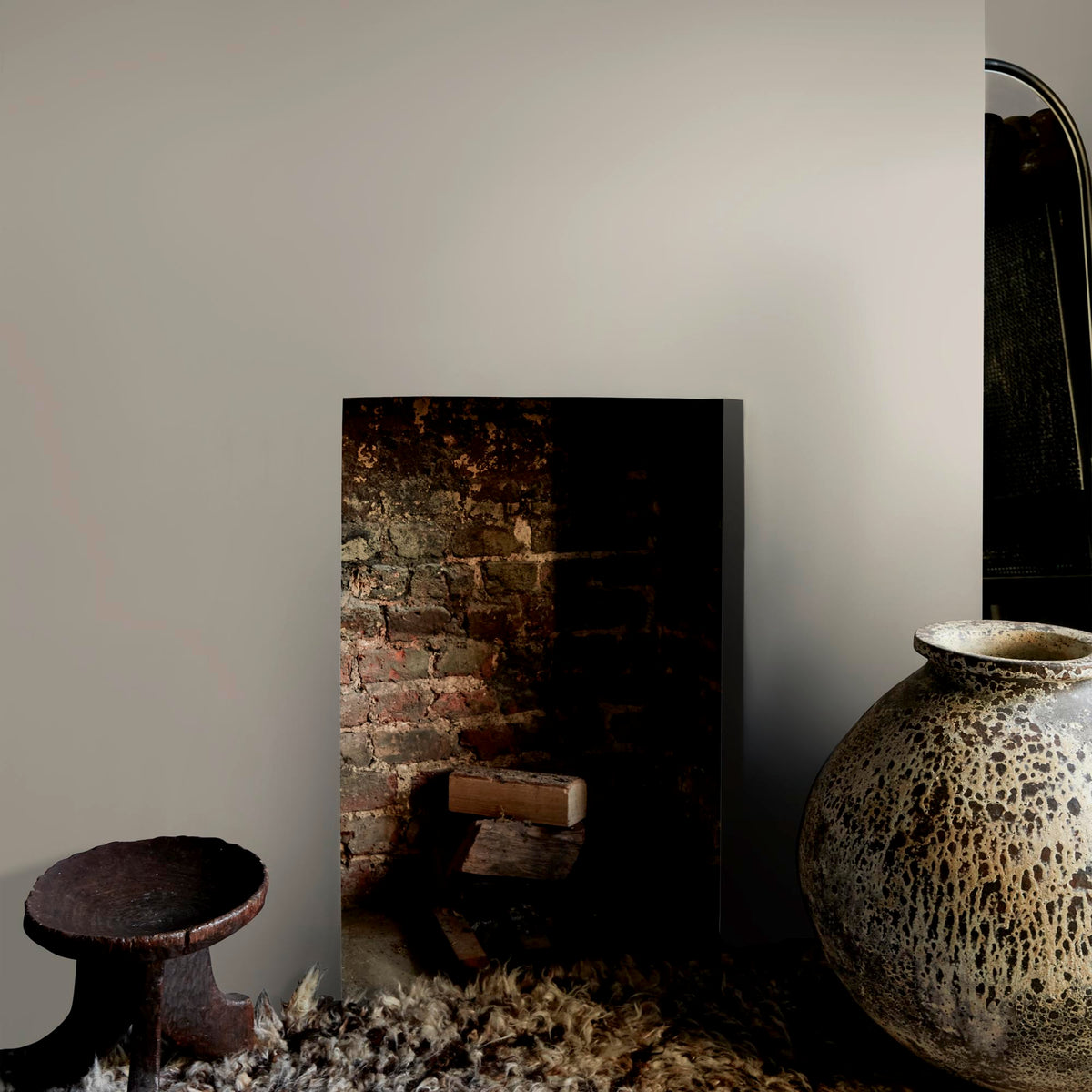 A minimalist fireplace painted in a warm beige paint colour, with a large ceramic vase in front of it.