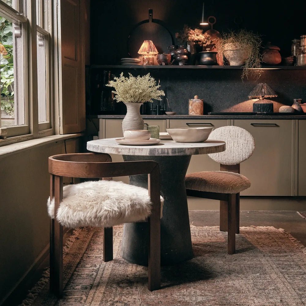 Loxford Sheepskin Dining Chair presents a curved brown wooden frame and a fluffy cream seat, styled at a round dining table beside a tall window.